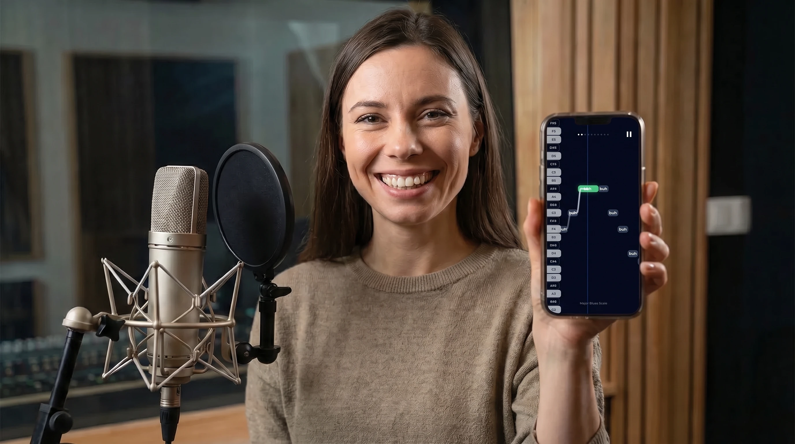 An image of a woman showing the screen of a phone with a vocal exercise on it, to the camera, and smiling, happy that she can practice her vocal technique every day.