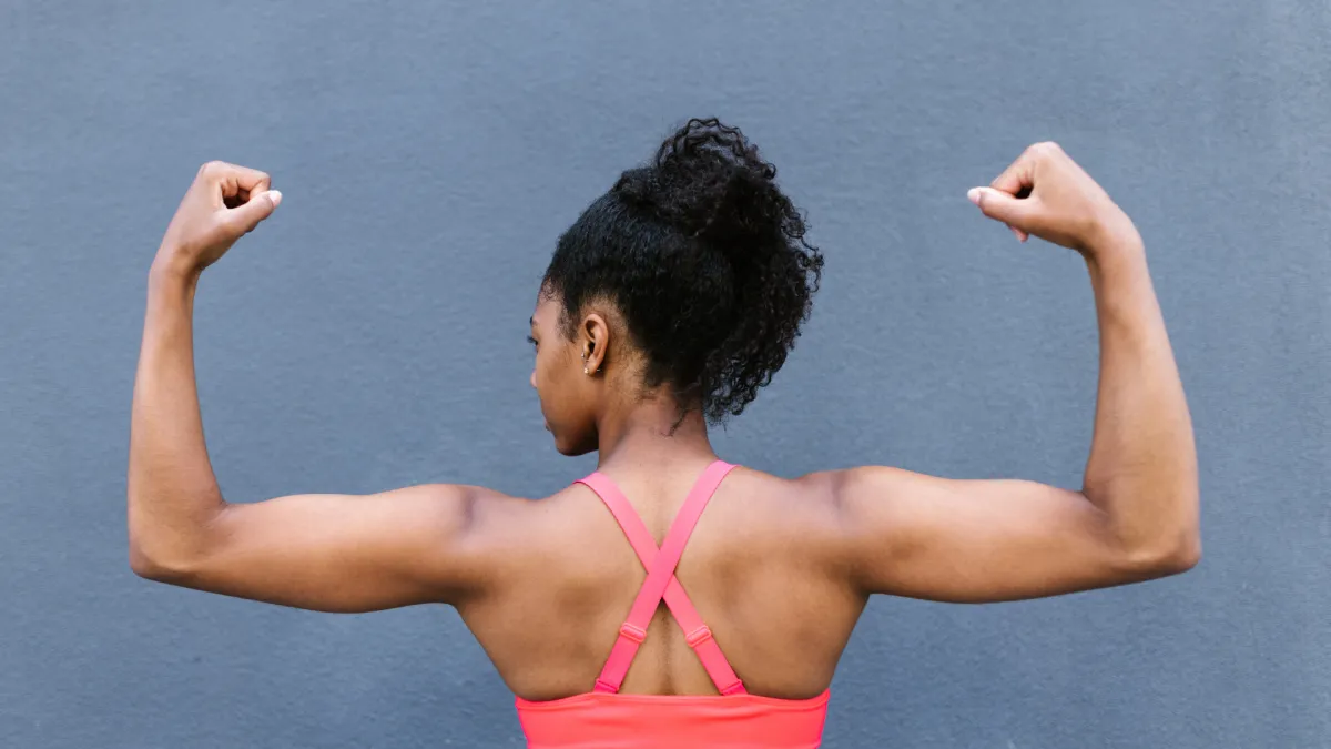 Woman seen from behind, flexing her back and shoulder muscles, representing continued strength training of the TA muscle